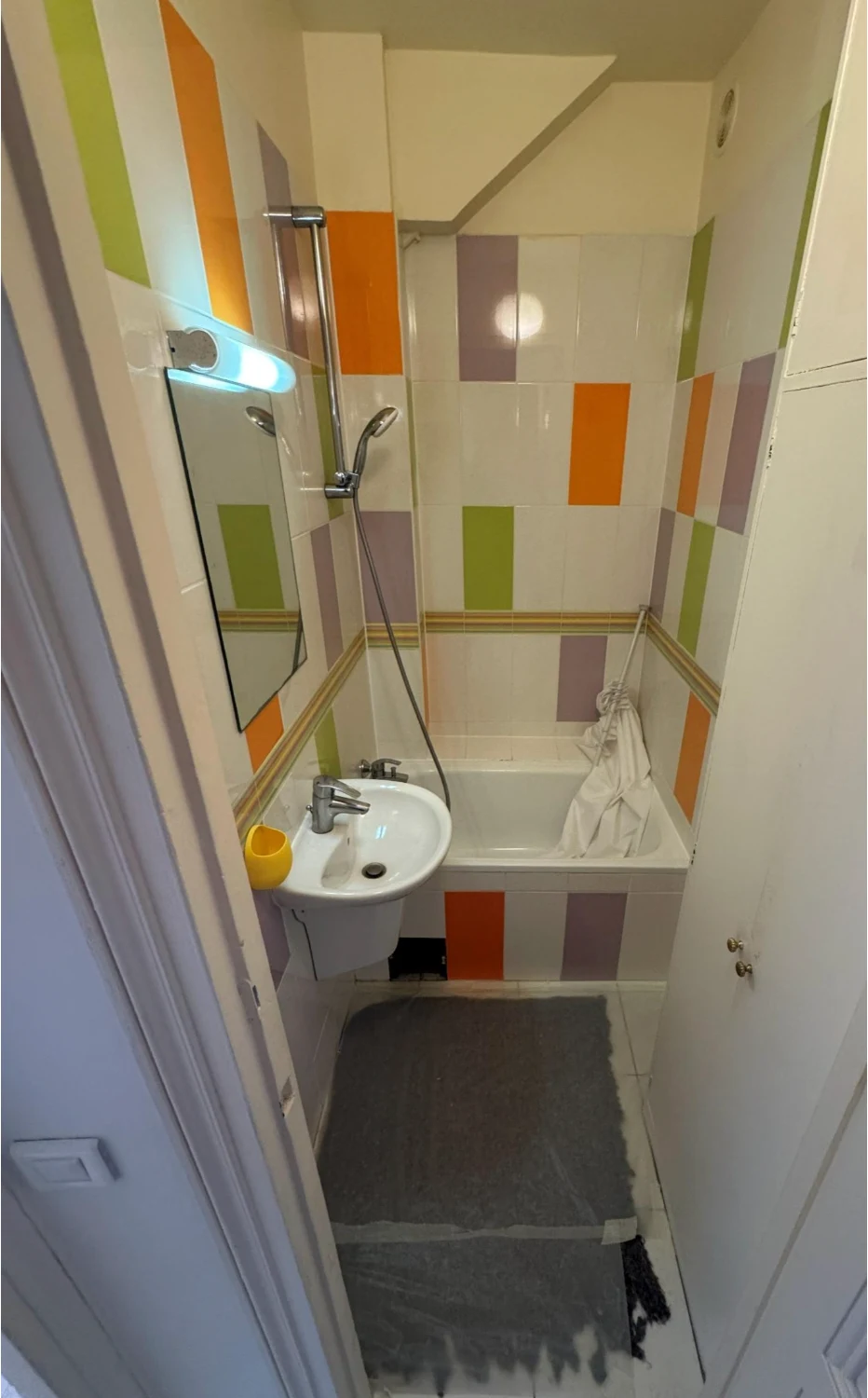 Avant rénovation : baignoire, petit lavabo et carrelage multicolore