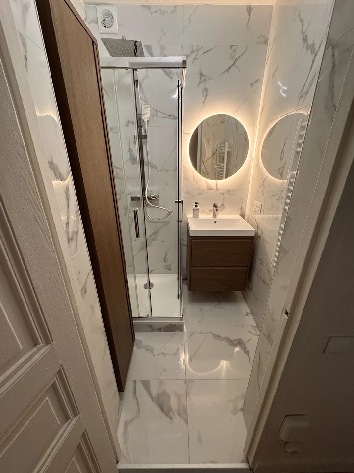Salle de bain effet marbre avec douche, meuble en bois et miroir rond lumineux
