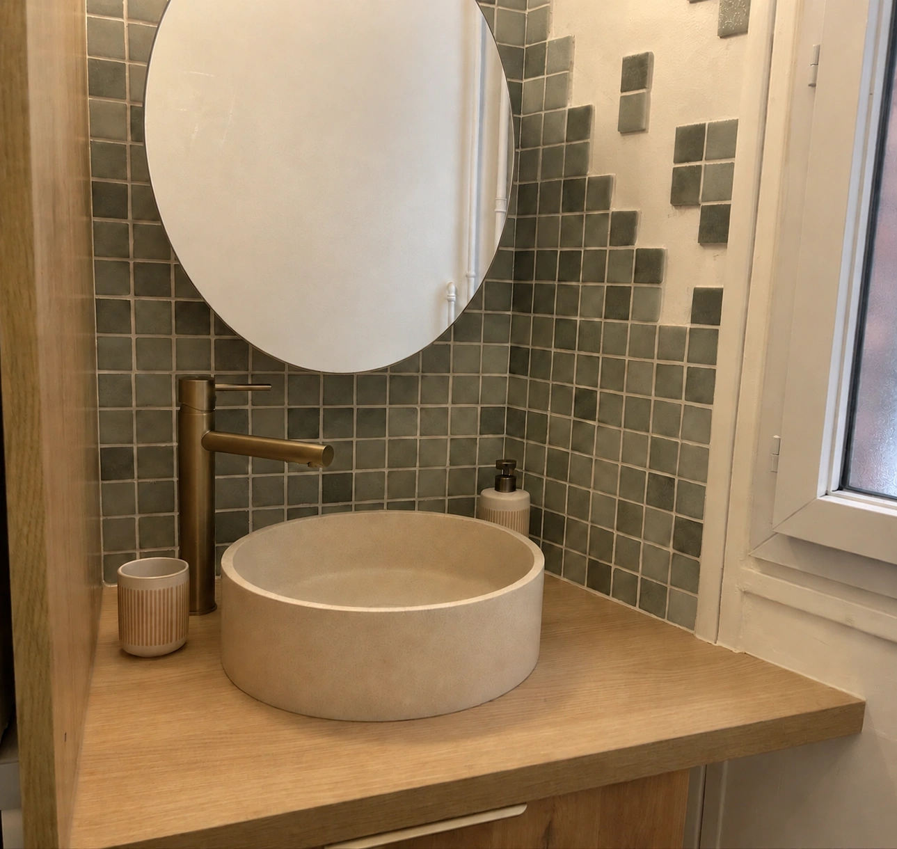 Réalisation SENOMA : vasque ronde, meuble en bois, robinetterie dorée et miroir sur carrelage vert